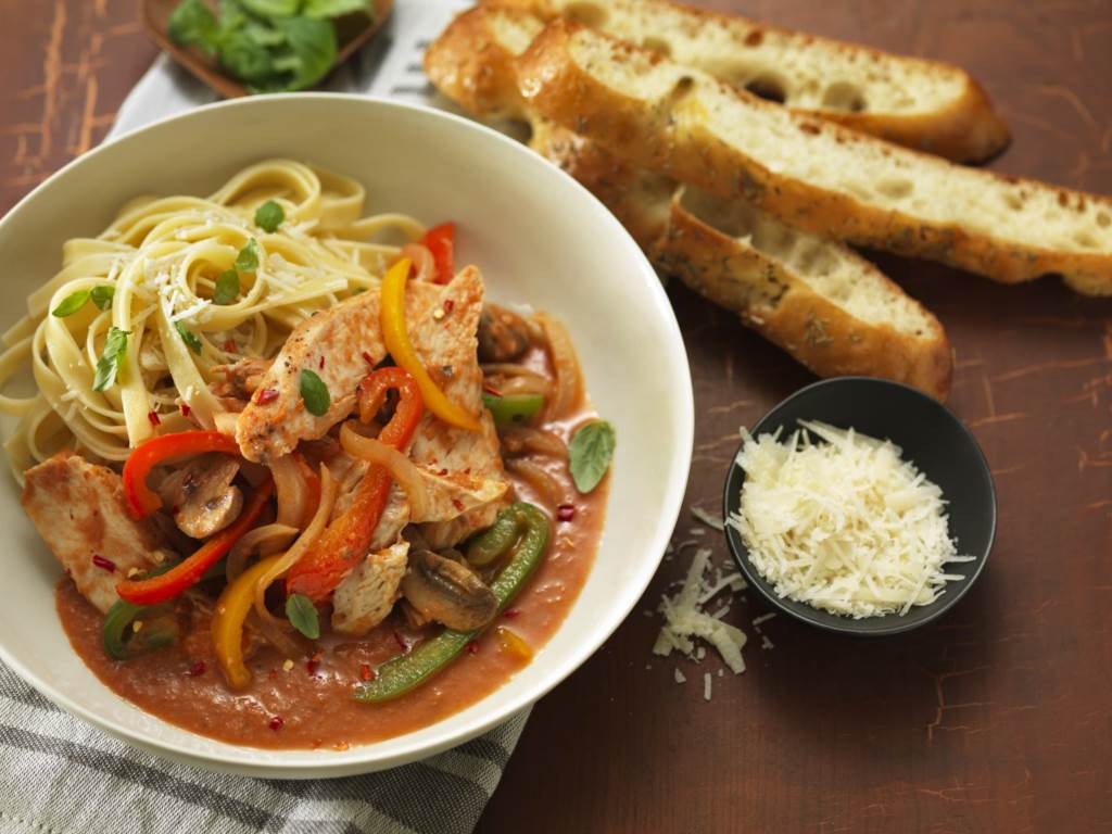 Chicken Cacciatore served in a bowl with bread on side and small bowl of grated cheese