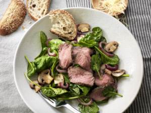 Warm Steak and Spinach Salad on plate with bread on side